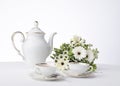 Classic white tea set with bouquet of white flowers and greenery on a white tablecloth