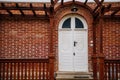 Classic wooden white carved oval door with glass inserts, brown canopy and lamp over porch, red block brick wall, entrance to Royalty Free Stock Photo