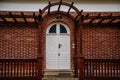 Classic wooden white carved oval door with glass inserts, brown canopy and lamp over porch, red block brick wall, entrance to Royalty Free Stock Photo