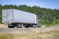 Classic work horse beige big rig semi truck transporting frozen cargo in reefer semi trailer driving on the scenic road with Royalty Free Stock Photo