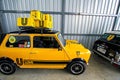 Classic yellow Mini Austin car is pictured parked in a garage, with a black wheel and a yellow box