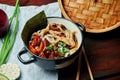Classical Asian soup with udon noodles, nori, shiitake mushrooms, and wok-fried chicken in black bowl on wooden background with