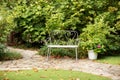 Classical decorative wrought iron garden bench. Cozy garden corner. Interior Patio of house with green plants in pots. White bench