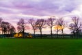 Classical dutch landscape of a grass field with trees and a farmer house, nacreous pink and purple clouds coloring the sky, rare Royalty Free Stock Photo