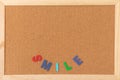 Classical plain brown cork board with wooden colorful SMILE letter at bottom of frame. Free copy space for text. Empty board backg