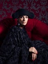 Classical portrait of woman wearing black hat end dress sitting on red sofa