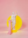 Classical statue holding a sphere stands on a pink background beside a yellow circular backdrop Royalty Free Stock Photo