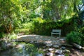 Classical white bench in beautiful tropical garden beside stream - green nature concept
