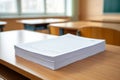 a classroom interior view shows empty wooden desks and chairs with a stack of lined papers Royalty Free Stock Photo