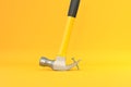 Claw hammer with yellow plastic handle pulling a nail out of a plank on yellow background