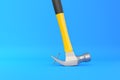 Claw hammer with yellow plastic handle pulling a nail out of a plank on blue background