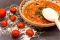 Clay bowl with traditional dish consist of tomatoes with grain noodles on slate and wooden spoon and ingredients near