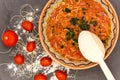 Clay bowl with traditional dish consist of tomatoes with grain noodles on slate and wooden spoon and ingredients near