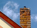 Isolated clay brick chimney with weathered and spalling surface. wood trim on house gable end wall. blue sky