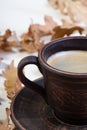 a clay cup with freshly brewed coffee and beautiful autumn oak leaves and acorns in a chaotic order on a white slate or Royalty Free Stock Photo