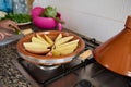 A clay dish on the stove, with slices potato on the kitchen counter. Woman cooking Moroccan tagine