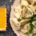 Clay plate of boiled dumplings sprinkled with dill herbs and ghee on black table background. High angle view. Cooking