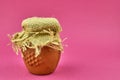 Clay pot with honey on a pink background.