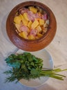 Clay pot with meat and potatoes for cooking roast. Greens and parsley on a plate. Russian national tradition Royalty Free Stock Photo