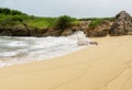 Clean beach sand with ocean waves plashing the shore rocks