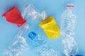 Clean crumpled plastic water bottles and colorful red and yellow disposable coffee cups ready for recycling isolated on blue backg