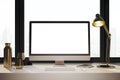 Clean designer desktop with empty white computer monitor, lamp, supplies and other items. Window with city view in the background Royalty Free Stock Photo