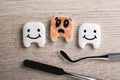 Clean and dirty plastic teeth with faces, dental tools on wooden table, flat lay