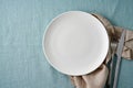 Clean empty white plate, fork and knife on pastel blue aquamarine linen tablecloth on table Royalty Free Stock Photo