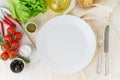 Clean empty white plate and vegetables on beige wooden background, top view, copy space Royalty Free Stock Photo