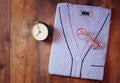 Clean folded man's pajama, vintage clock and glasses over wooden background. top view