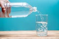 Clean healthy cool water is pouring into a glass from a plastic bottle on a blue background Royalty Free Stock Photo