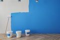 Clean interior with blue paint on concrete wall, painting tools, ladder, lamps and wooden flooring. Repairs concept.