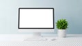A modern computer setup with a blank screen, keyboard, mouse, and a green plant on a white desk against a light blue wall for Royalty Free Stock Photo
