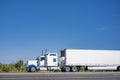 Clean powerful classic white big rig semi truck tractor transporting cargo in refrigerator semi trailer driving on the highway Royalty Free Stock Photo