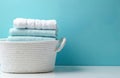Clean soft towels, white and blue, neatly folded in woven basket. Fresh laundry stack on white surface against vibrant blue Royalty Free Stock Photo