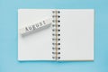 Clean spiral note book for notes and messages and august wooden calendar bar on blue background. Minimal business flat lay
