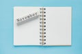 Clean spiral note book for notes and messages and november wooden calendar bar on blue background. Minimal business flat lay