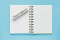 Clean spiral note book for notes and messages and september wooden calendar bar on blue background. Minimal business flat lay