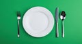 Minimalist Overhead Shot of White Plate with Silverware on Vibrant Green Background Royalty Free Stock Photo