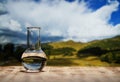 Clean water in a glass laboratory flask on wooden table on mountain background. Ecological concept, the test of purity Royalty Free Stock Photo
