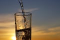 Clean water pouring into drinking glass on sunset sky background Royalty Free Stock Photo