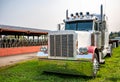 Clean classic big rig semi truck tractor with flat bed semi trailer standing on the farm with field and cow stall Royalty Free Stock Photo