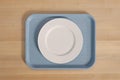 Clean white dinner plate centered on rectangular blue cafeteria tray resting on light brown wooden table surface from above simple Royalty Free Stock Photo
