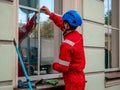 Cleaner with mop and accessories  prepares to wash windows in historical architecture building. Worker in branded red overalls, Royalty Free Stock Photo