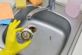 Cleaner in rubber gloves shows waste in the plughole protector of a kitchen sink