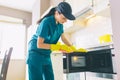 Cleaner stands in kitchen and cleans surface of microvawe owen. She does it with gloves and rag. Girl is calm and Royalty Free Stock Photo