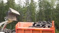 Cleaning the area: the bucket of the escavator with a large number of tires dumps garbage into the body. Illegal dump in the woods Royalty Free Stock Photo