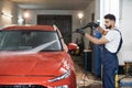 Handsome young bearded man worker washing modern red luxury car under high pressure Royalty Free Stock Photo