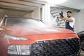 Handsome young bearded man worker washing modern red luxury car under high pressure Royalty Free Stock Photo