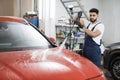Handsome man worker washing modern red car hood under high pressure water in car wash service Royalty Free Stock Photo